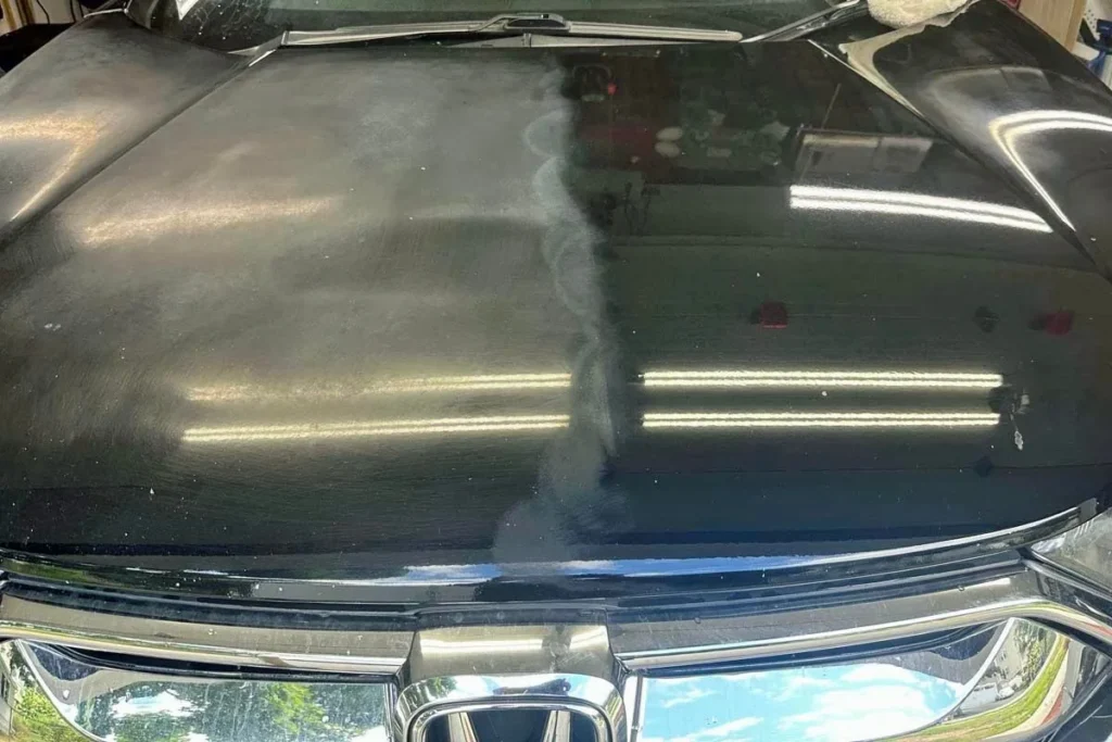 Paint correction in Stoneham MA a technician polishing black car hood to remove oxidation and swirl marks.